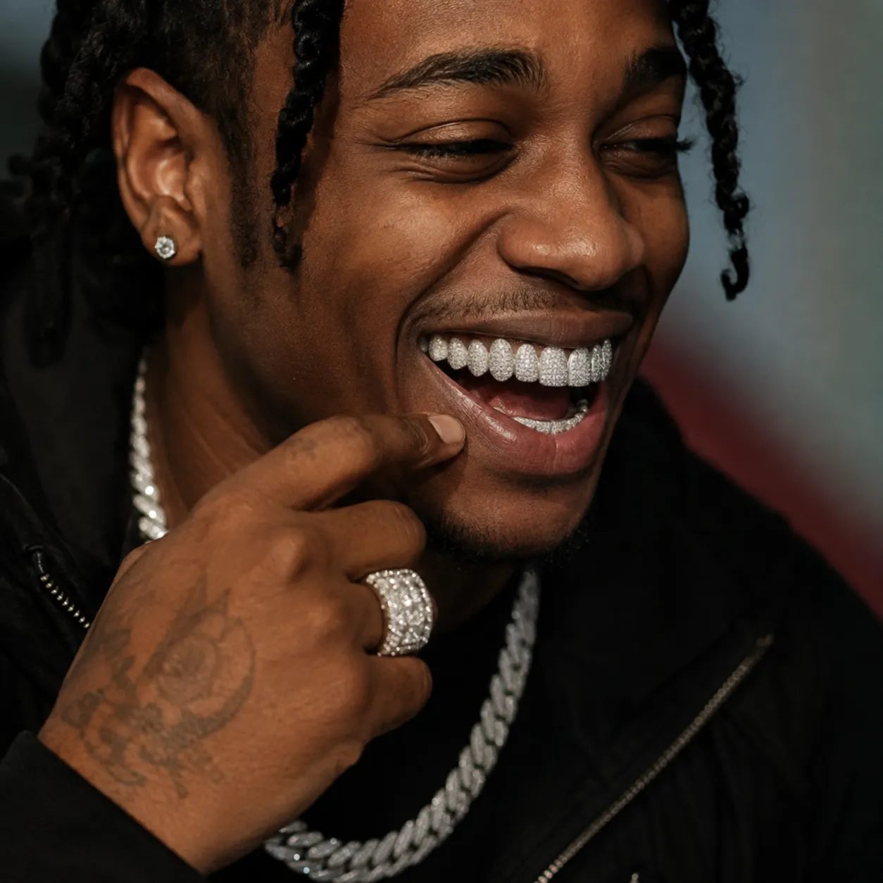 A man smiling to reveal a fully iced-out moissanite grillz set on his upper teeth, with a diamond ring and cuban link chain
